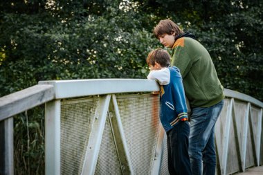 İki çocuk bir köprüde durup, uzaklığa bakıyorlar. Sahne, doğa ile çevrili huzurlu bir anı paylaşırken sessiz bir yansıma anı yakalıyor..