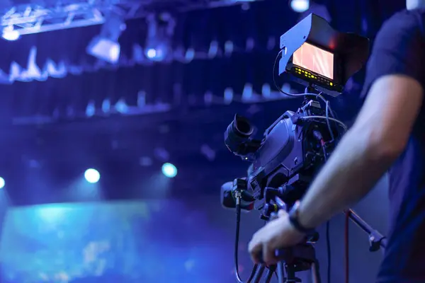 Bir videograf canlı bir olay sırasında, canlı mavi sahne ışıklandırması ve bulanık arka planı ile dinamik bir atmosfer yaratan profesyonel bir kamera kullanır. Kamera ekranı devam eden görüntüyü gösterir