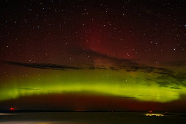 Gece gökyüzünü aydınlatan kırmızı ve yeşil auroraların göz kamaştırıcı bir görüntüsü ve arka planda parlayan yıldızlar. Canlı göksel olay büyüleyici, ruhani bir atmosfer yaratır..