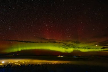 Gece gökyüzünü aydınlatan kırmızı ve yeşil auroraların göz kamaştırıcı bir görüntüsü ve arka planda parlayan yıldızlar. Canlı göksel olay büyüleyici, ruhani bir atmosfer yaratır..
