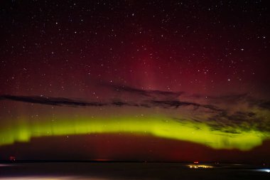 Gece gökyüzünü aydınlatan kırmızı ve yeşil auroraların göz kamaştırıcı bir görüntüsü ve arka planda parlayan yıldızlar. Canlı göksel olay büyüleyici, ruhani bir atmosfer yaratır..