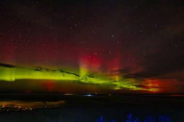 Gece gökyüzünü aydınlatan kırmızı ve yeşil auroraların göz kamaştırıcı bir görüntüsü ve arka planda parlayan yıldızlar. Canlı göksel olay büyüleyici, ruhani bir atmosfer yaratır..