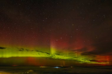 Gece gökyüzünü aydınlatan kırmızı ve yeşil auroraların göz kamaştırıcı bir görüntüsü ve arka planda parlayan yıldızlar. Canlı göksel olay büyüleyici, ruhani bir atmosfer yaratır..