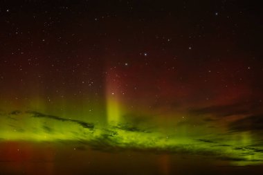 Gece gökyüzünü aydınlatan kırmızı ve yeşil auroraların göz kamaştırıcı bir görüntüsü ve arka planda parlayan yıldızlar. Canlı göksel olay büyüleyici, ruhani bir atmosfer yaratır..