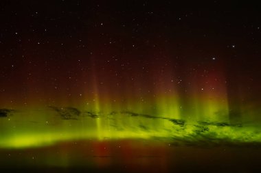 Gece gökyüzünü aydınlatan kırmızı ve yeşil auroraların göz kamaştırıcı bir görüntüsü ve arka planda parlayan yıldızlar. Canlı göksel olay büyüleyici, ruhani bir atmosfer yaratır..