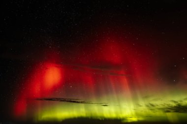 Gece gökyüzünü aydınlatan kırmızı ve yeşil auroraların göz kamaştırıcı bir görüntüsü ve arka planda parlayan yıldızlar. Canlı göksel olay büyüleyici, ruhani bir atmosfer yaratır..