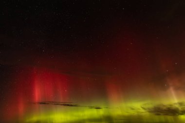 Gece gökyüzünü aydınlatan kırmızı ve yeşil auroraların göz kamaştırıcı bir görüntüsü ve arka planda parlayan yıldızlar. Canlı göksel olay büyüleyici, ruhani bir atmosfer yaratır..