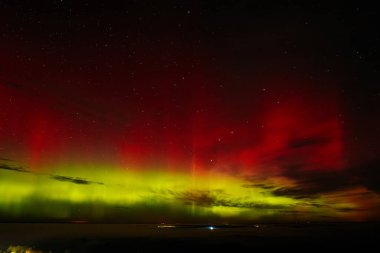 Gece gökyüzünü aydınlatan kırmızı ve yeşil auroraların göz kamaştırıcı bir görüntüsü ve arka planda parlayan yıldızlar. Canlı göksel olay büyüleyici, ruhani bir atmosfer yaratır..