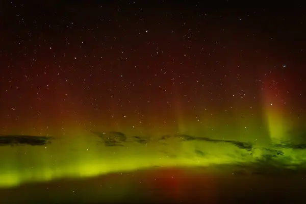 Gece gökyüzünü aydınlatan kırmızı ve yeşil auroraların göz kamaştırıcı bir görüntüsü ve arka planda parlayan yıldızlar. Canlı göksel olay büyüleyici, ruhani bir atmosfer yaratır..