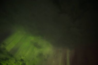 Aurora Borealis 'in barışçıl bir görüntüsü yıldızlı gece gökyüzünde yumuşak yeşil ışık saçar. Nazik parıltı karanlık arka plana karışıyor, dingin ve ruhani bir atmosfer yaratıyor..