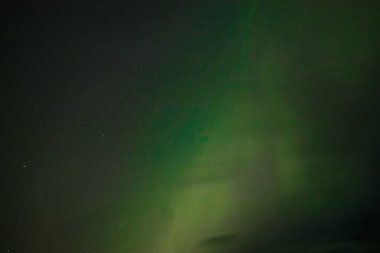  Yumuşak yeşil aurora borealis, yıldızlı bir gece gökyüzünde usulca süzülür ve dingin ve göksel bir manzara yaratır. Uzak yıldızlar, kuzey ışıklarının sönük parıltısında parıldıyor..