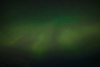  Yumuşak yeşil aurora borealis, yıldızlı bir gece gökyüzünde usulca süzülür ve dingin ve göksel bir manzara yaratır. Uzak yıldızlar, kuzey ışıklarının sönük parıltısında parıldıyor..
