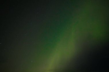  Yumuşak yeşil aurora borealis, yıldızlı bir gece gökyüzünde usulca süzülür ve dingin ve göksel bir manzara yaratır. Uzak yıldızlar, kuzey ışıklarının sönük parıltısında parıldıyor..