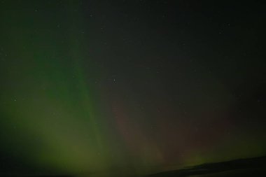  Yumuşak yeşil aurora borealis, yıldızlı bir gece gökyüzünde usulca süzülür ve dingin ve göksel bir manzara yaratır. Uzak yıldızlar, kuzey ışıklarının sönük parıltısında parıldıyor..