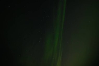  Yumuşak yeşil aurora borealis, yıldızlı bir gece gökyüzünde usulca süzülür ve dingin ve göksel bir manzara yaratır. Uzak yıldızlar, kuzey ışıklarının sönük parıltısında parıldıyor..