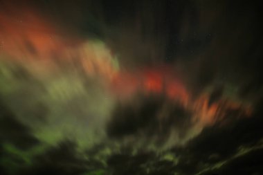 Aurora Borealis 'in nefes kesici görüntüsü gece gökyüzünü canlı kırmızı ve yeşil renklerle aydınlatıyor. Kara bulutlar kısmen karanlık Işıldayan ışıklar