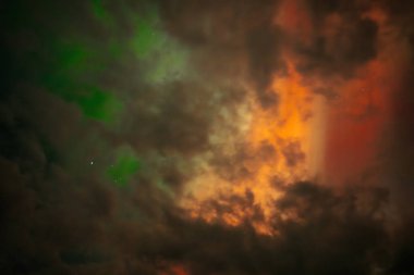 Aurora Borealis 'in nefes kesici görüntüsü gece gökyüzünü canlı kırmızı ve yeşil renklerle aydınlatıyor. Kara bulutlar kısmen karanlık Işıldayan ışıklar