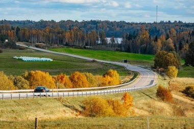 Sonbaharda manzaralı bir kır manzarası, sarılı, turuncu ve yeşil yapraklarla çevrili dolambaçlı bir yol..