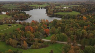 Bir dron, arka planında dingin bir göl bulunan canlı sarı ve kırmızı ağaçların nefes kesici sonbahar sahnesini yakalar. Renkli yapraklar durgun suyla çok güzel zıtlaşıyor.