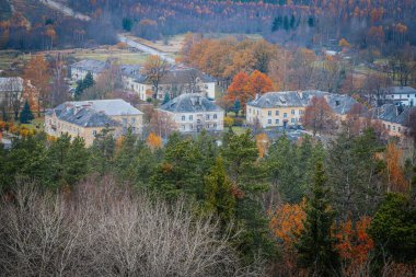 Uçsuz bucaksız bir sonbahar ormanının içine yerleşmiş küçük bir kasabanın havadan görünüşü. Ağaçlar canlı turuncu ve sarı yapraklar sergiliyor. Kasabanın binaları doğal ortama uyum sağlıyor. Zilaiskalns