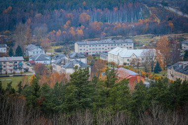 Uçsuz bucaksız bir sonbahar ormanının içine yerleşmiş küçük bir kasabanın havadan görünüşü. Ağaçlar canlı turuncu ve sarı yapraklar sergiliyor. Kasabanın binaları doğal ortama uyum sağlıyor. Zilaiskalns