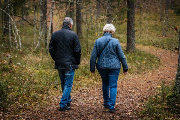 People walk up a forest path covered in autumn leaves. They are dressed warmly for the season, surrounded by fall foliage