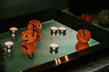 Miniature orange pumpkin buckets with jack-o'-lantern faces and tealight candles arranged on a reflective glass surface, creating a spooky Halloween ambiance. clipart