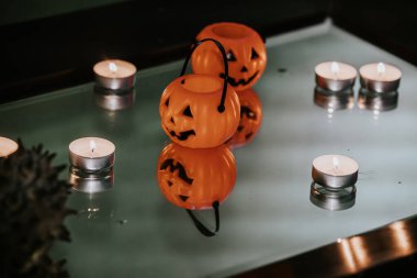 Miniature orange pumpkin buckets with jack-o'-lantern faces and tealight candles arranged on a reflective glass surface, creating a spooky Halloween ambiance. clipart