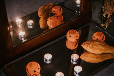 Miniature orange pumpkin buckets with jack-o'-lantern faces and tealight candles arranged on a reflective glass surface, creating a spooky Halloween ambiance. clipart