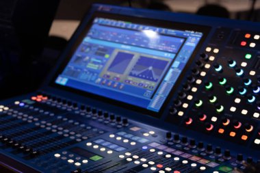 Etkileşimli bir ekran ve renkli LED ışıklı düğmeler içeren dijital bir ses karıştırma konsolunun yakın görüntüsü. Ses mühendisliği, müzik üretimi ve canlı performans ayarları için ideal, yüksek teknoloji ve dinamik bir atmosfer yakalamak.