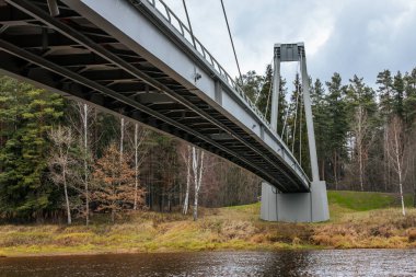 Yapısal kabloların ve modern asma köprünün metal sütunlarının bulutlu bir gökyüzüne yakın görüntüsü. Kablolar gergin, uzun çelik destekleri birbirine bağlıyor..
