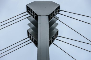 Yapısal kabloların ve modern asma köprünün metal sütunlarının bulutlu bir gökyüzüne yakın görüntüsü. Kablolar gergin, uzun çelik destekleri birbirine bağlıyor..