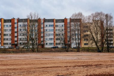Tuğla ve alçı cepheli kentsel apartman manzarası. Ön planda çıplak ağaçlar duruyor, yapraksız dalları binanın pencerelerine karşı katıksız bir kontrast oluşturuyor..