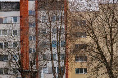 Tuğla ve alçı cepheli kentsel apartman manzarası. Ön planda çıplak ağaçlar duruyor, yapraksız dalları binanın pencerelerine karşı katıksız bir kontrast oluşturuyor..