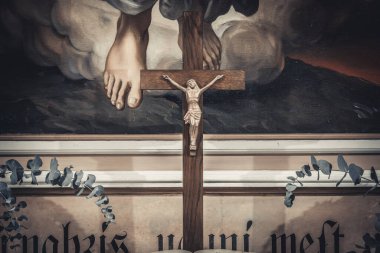 Kilisenin sunağında açık bir İncil, ahşap bir haç ve her iki tarafta da çiçek aranjmanları var. Arka planda dini bir tablo ve dekoratif bir senaryo yer alıyor.