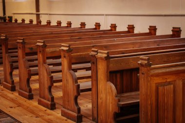 Rows of beautifully crafted wooden pews inside a church, illuminated by warm, natural light. The polished wood grain and intricate details reflect a classic, timeless design clipart