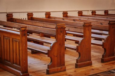 Rows of beautifully crafted wooden pews inside a church, illuminated by warm, natural light. The polished wood grain and intricate details reflect a classic, timeless design clipart