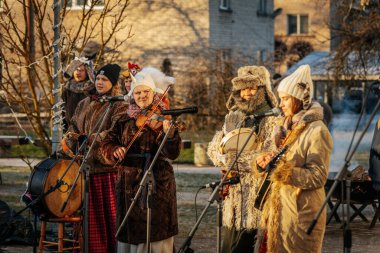 Bir grup kostümlü katılımcı, geleneksel kıyafet ve festival maskeleriyle Kış Gündönümünü kutluyor, kültürel mirası ve mevsimsel keyfi ele geçiriyorlar. 12.21.2024 Balvi, Letonya