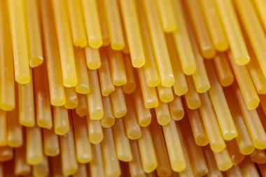 Pişmemiş kuru spagetti eriştelerinin yakın çekimleri pürüzsüz dokularını ve parlak altın sarısı renklerini gözler önüne seriyor. Mutfak ve yemek temalı görüntüler için mükemmel..