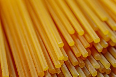 Pişmemiş kuru spagetti eriştelerinin yakın çekimleri pürüzsüz dokularını ve parlak altın sarısı renklerini gözler önüne seriyor. Mutfak ve yemek temalı görüntüler için mükemmel..