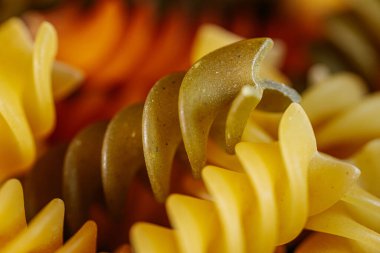 Renkli, turuncu, sarı ve yeşil renklerde, dokusunu ve şeklini vurgulayan kuru sarmal makarna. Gıda ile ilgili temalar ve mutfak içeriği için ideal.