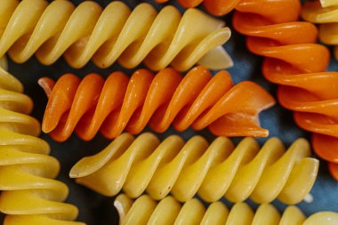 Renkli, turuncu, sarı ve yeşil renklerde, dokusunu ve şeklini vurgulayan kuru sarmal makarna. Gıda ile ilgili temalar ve mutfak içeriği için ideal.