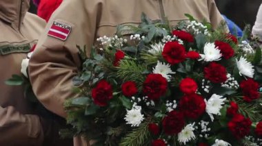 Resmi bir tören sırasında ellerinde mumlarla Letonyalı öğrencilerin yakın çekimleri. Bir buket kırmızı ve beyaz çiçek, anma ve ulusal gururu simgeler..