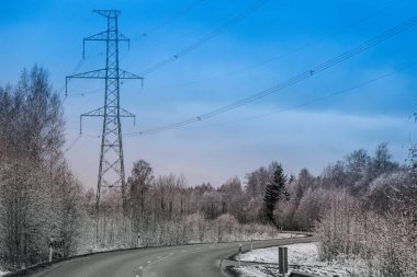 Yüksek voltajlı bir elektrik direği bulutlu mavi bir gökyüzüne karşı duruyor ve çoklu elektrik hatlarını destekliyor. Çelik kafes yapısı endüstriyel enerji altyapısını vurguluyor.