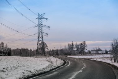 Yüksek voltajlı bir elektrik direği bulutlu mavi bir gökyüzüne karşı duruyor ve çoklu elektrik hatlarını destekliyor. Çelik kafes yapısı endüstriyel enerji altyapısını vurguluyor.