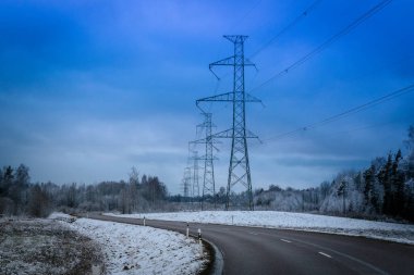 Yüksek voltajlı bir elektrik direği bulutlu mavi bir gökyüzüne karşı duruyor ve çoklu elektrik hatlarını destekliyor. Çelik kafes yapısı endüstriyel enerji altyapısını vurguluyor.