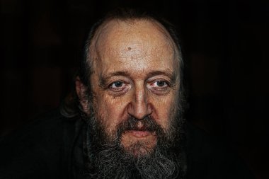 Derin kırışıklıkları, uzun sakalı ve delici gözleri olan yaşlı bir adamın dramatik yakın plan portresi. Karanlık arka plan, yoğun ve duygusal ifadeyi güçlendirir..