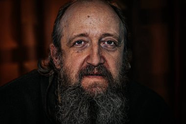 Derin kırışıklıkları, uzun sakalı ve delici gözleri olan yaşlı bir adamın dramatik yakın plan portresi. Karanlık arka plan, yoğun ve duygusal ifadeyi güçlendirir..