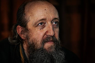 Derin kırışıklıkları, uzun sakalı ve delici gözleri olan yaşlı bir adamın dramatik yakın plan portresi. Karanlık arka plan, yoğun ve duygusal ifadeyi güçlendirir..