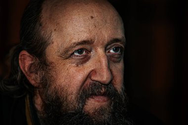 Derin kırışıklıkları, uzun sakalı ve delici gözleri olan yaşlı bir adamın dramatik yakın plan portresi. Karanlık arka plan, yoğun ve duygusal ifadeyi güçlendirir..
